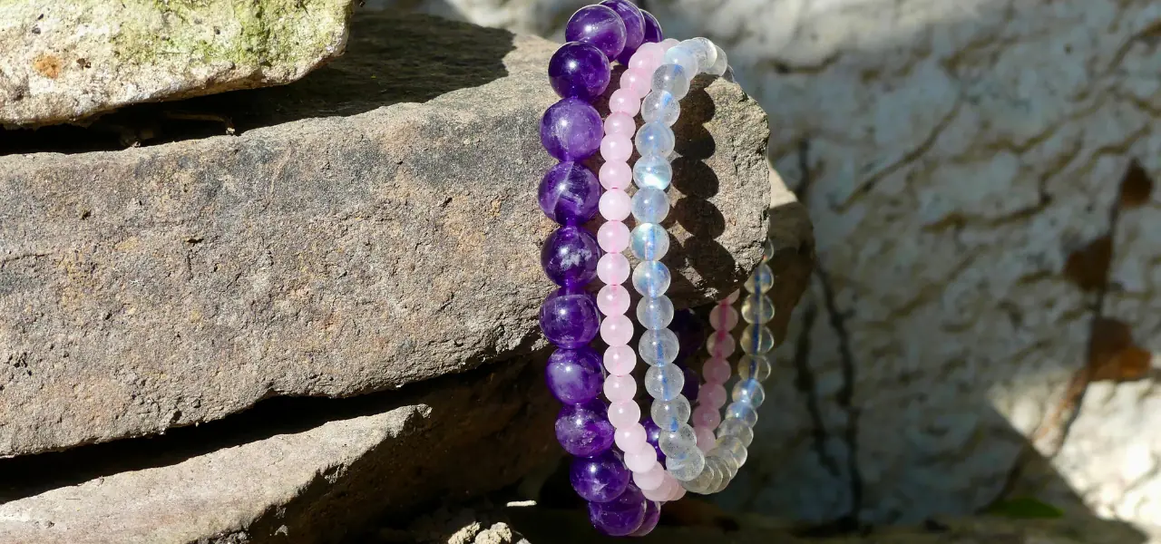 Plusieurs bijoux en pierre naturelle de couleur violet et rose posés sur une grosse pierre