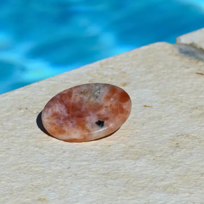 un galet anti stress en pierre de soleil posé au bord d'une piscine en gros plan