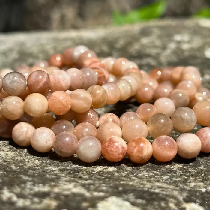 Bracelet pierre de soleil 6 mm posé sur une grosse pierre, dans un jardin