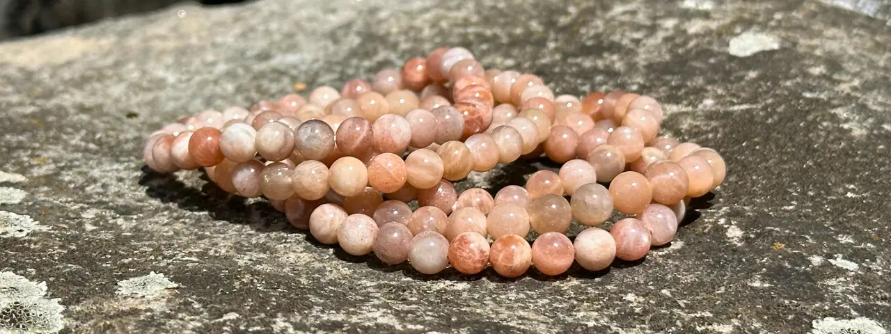 Bracelet pierre de soleil 6 mm posé sur une grosse pierre, dans un jardin