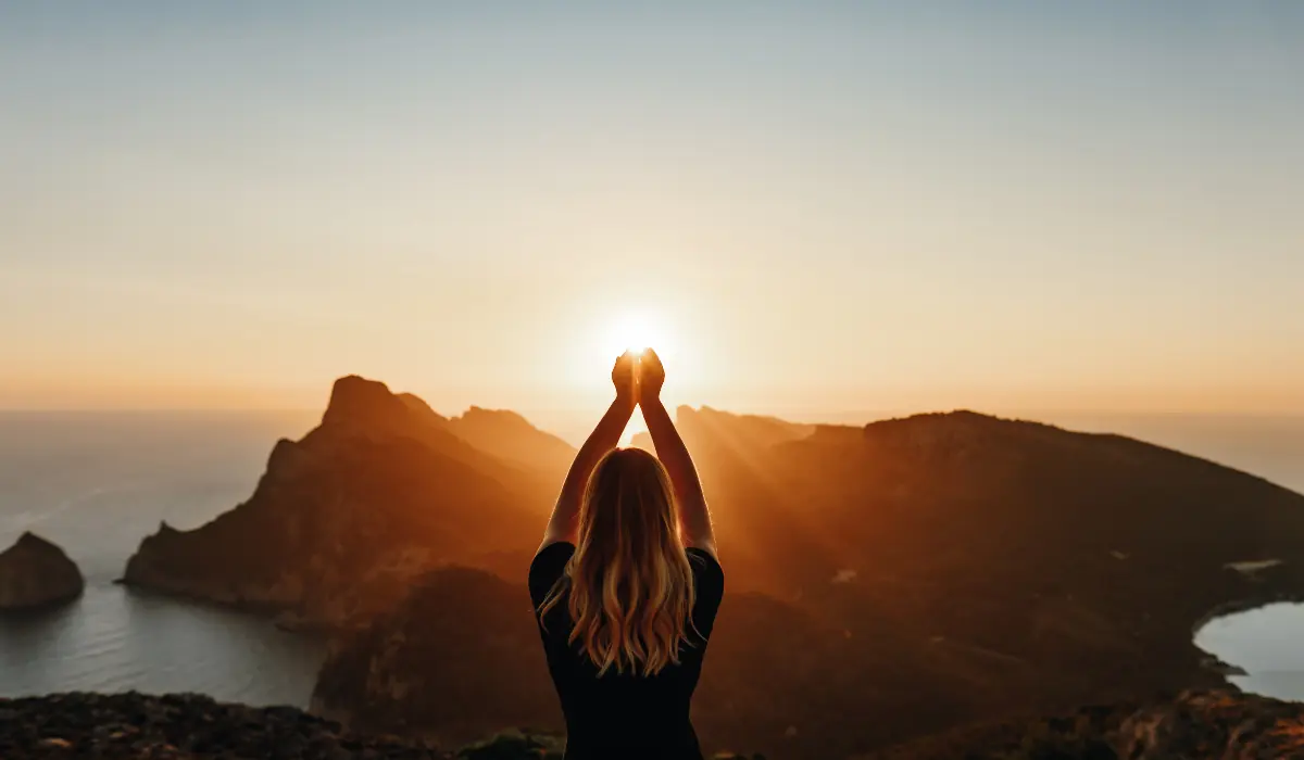 Jeune femme cachant un soleil couchant avec ses mains pour illustrer la synchronicité