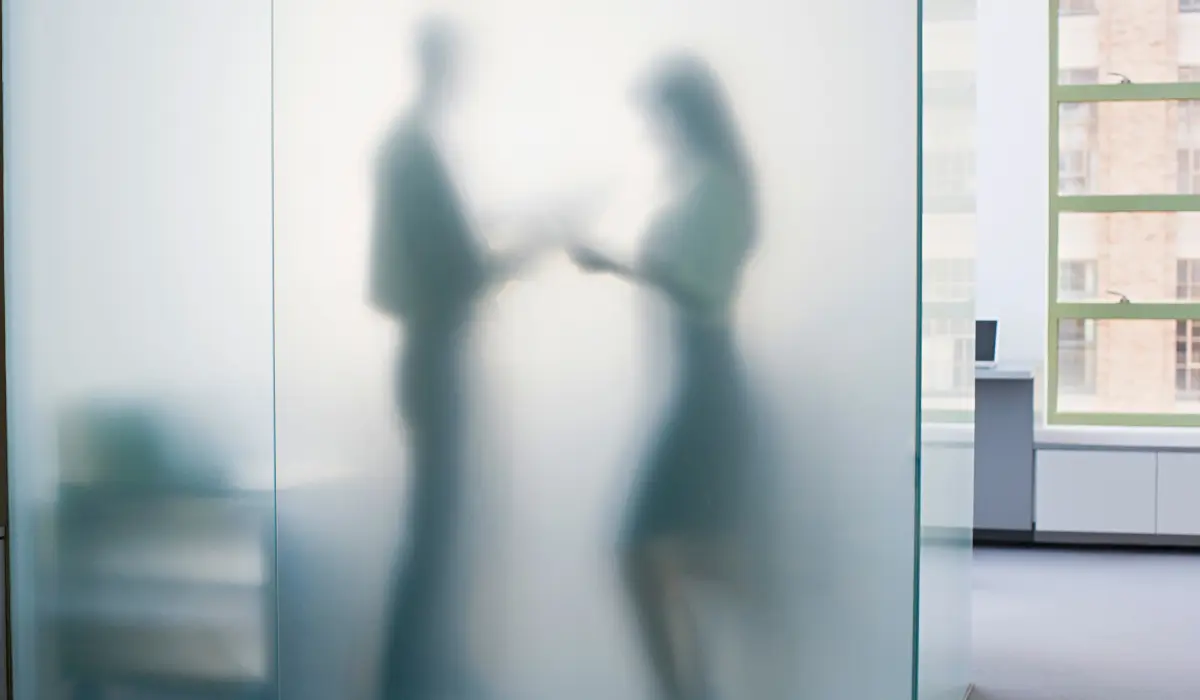 Un homme et une femme au travail discutant derrière un panneau en verre