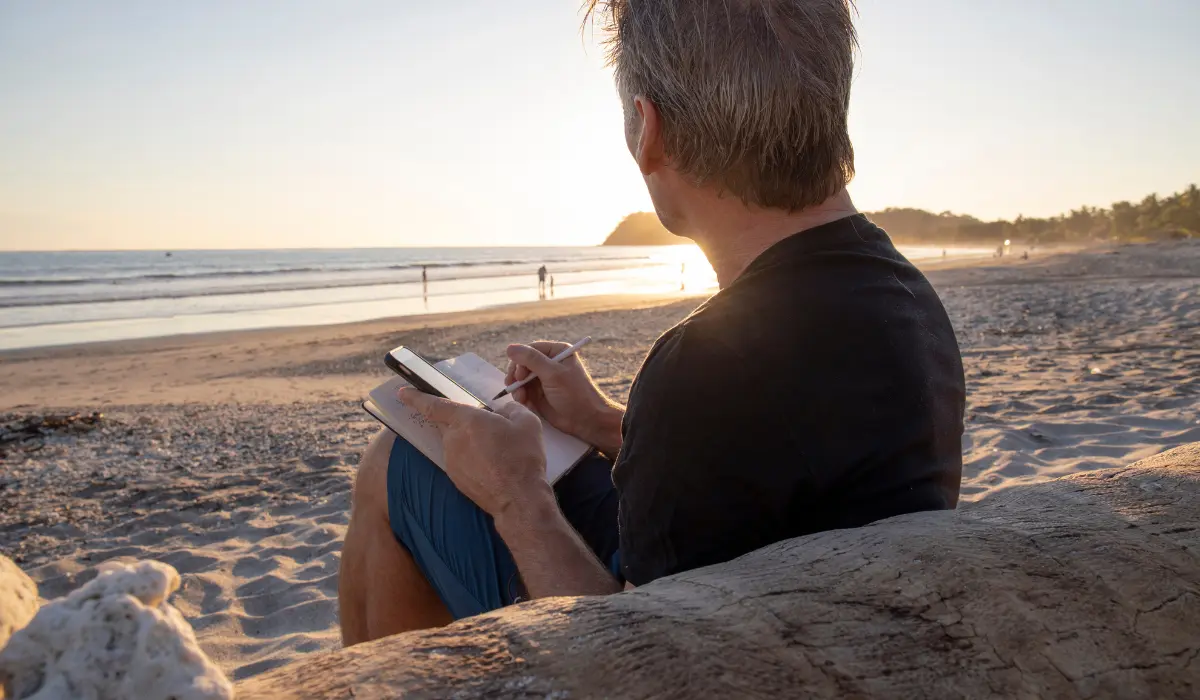 Homme à la plage en train d'écrire dans un carnet, une action consciente