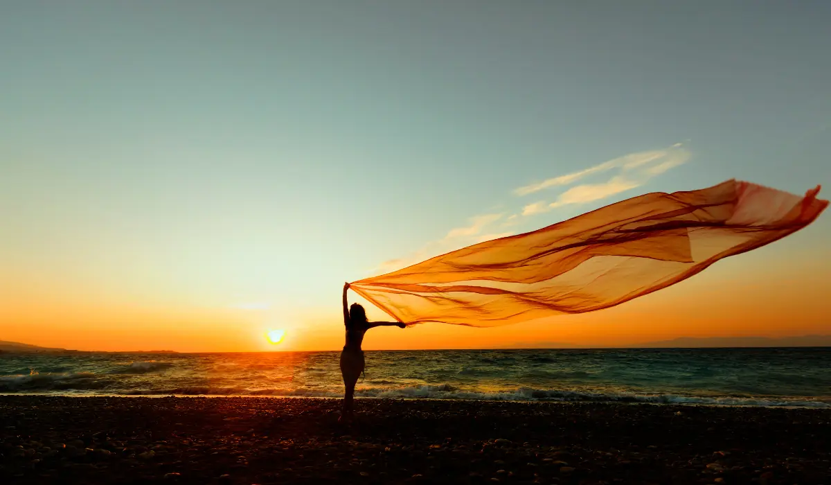 Jeune femme tenant un large voile près de la mer, au vent