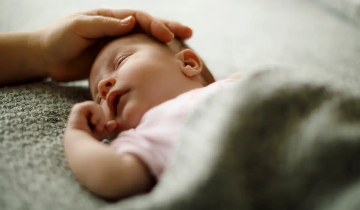 Un bébé endormi avec la main de sa mère sur la tête