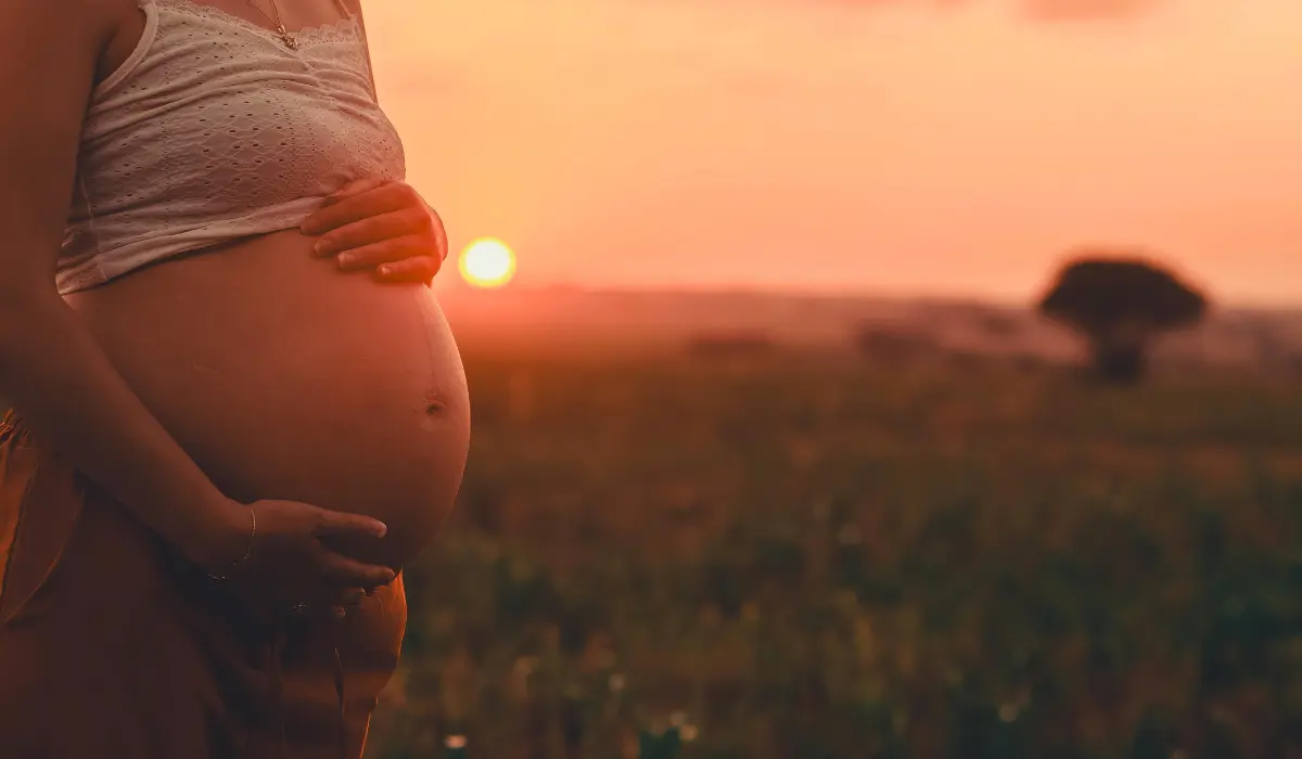 une femme enceinte devant un soleil couchant