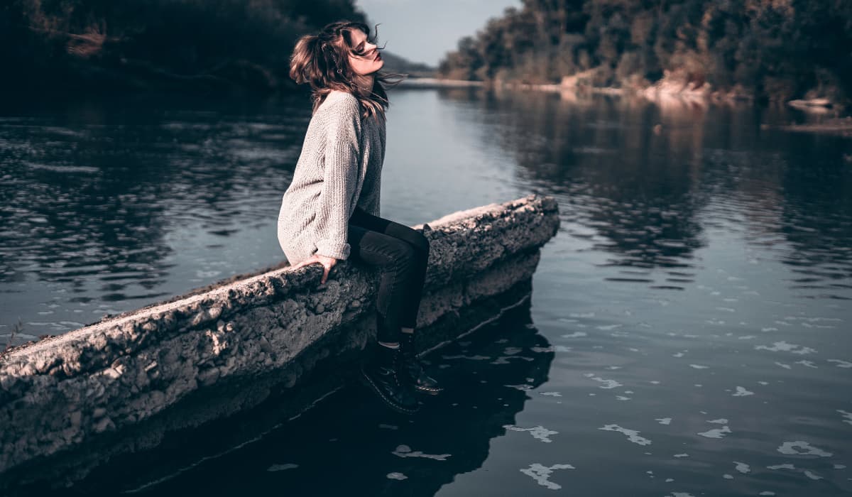jeune femme assise sur un muret près d'un lac