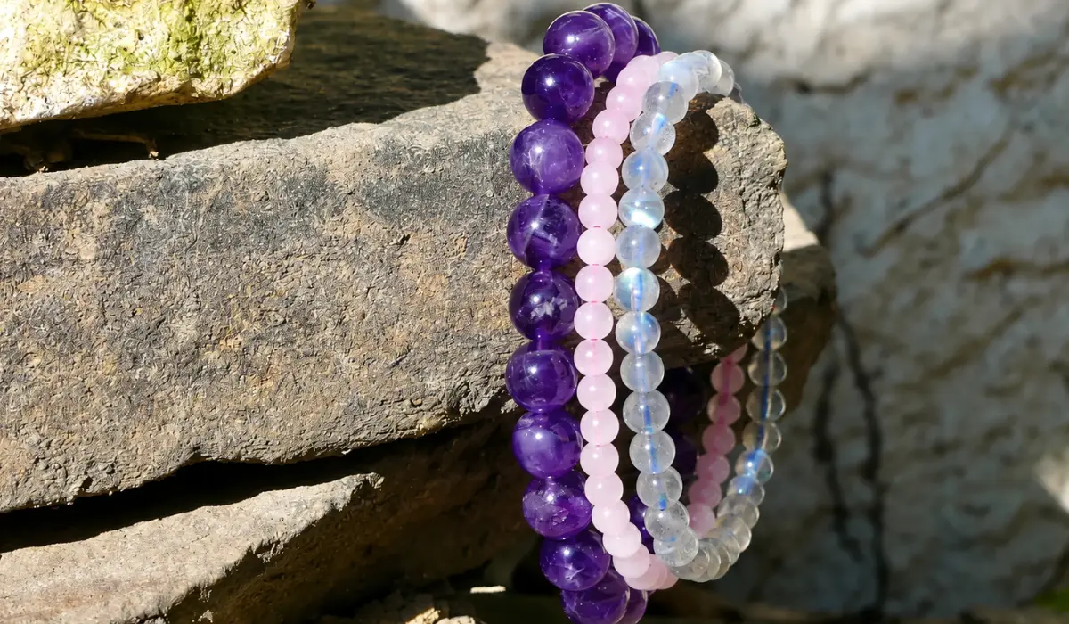 Plusieurs bijoux en pierre naturelle de couleur violet et rose posés sur une grosse pierre